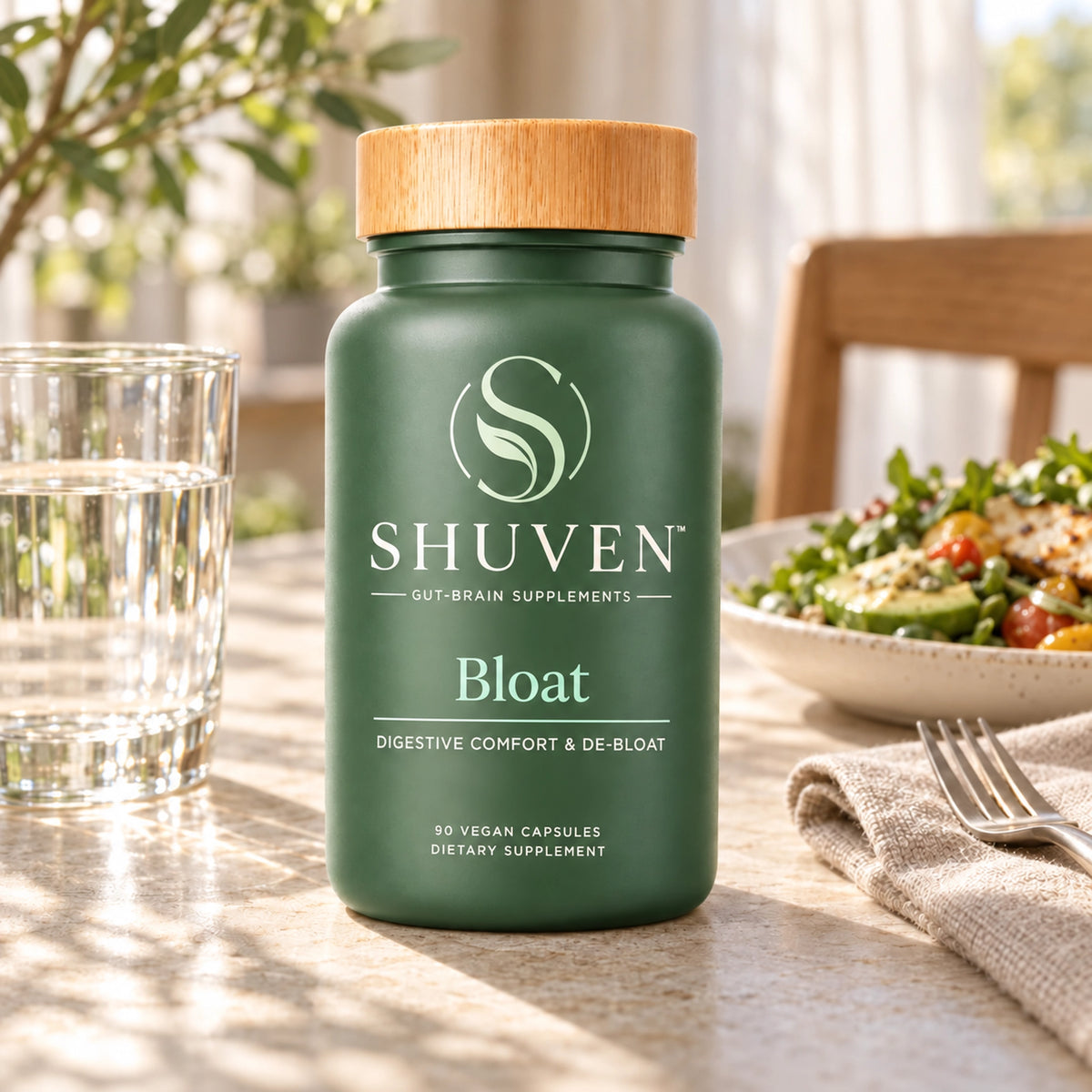 Shuven Bloat supplement bottle on dining table with water glass and salad bowl