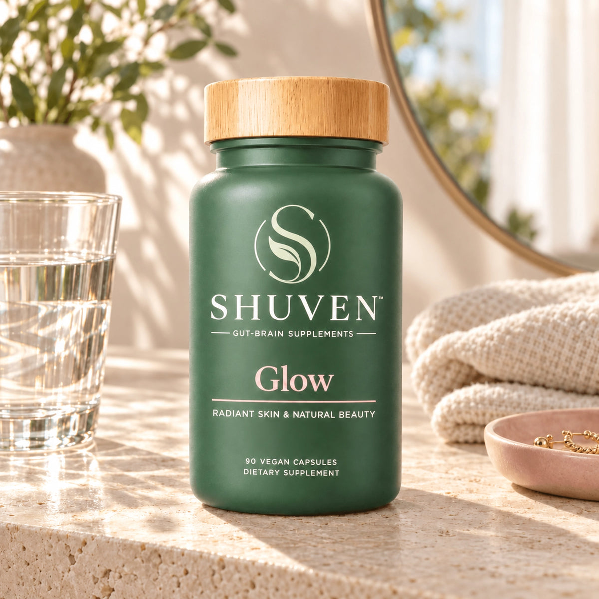 Shuven Glow supplement bottle on marble counter with capsules, water glass, and towels